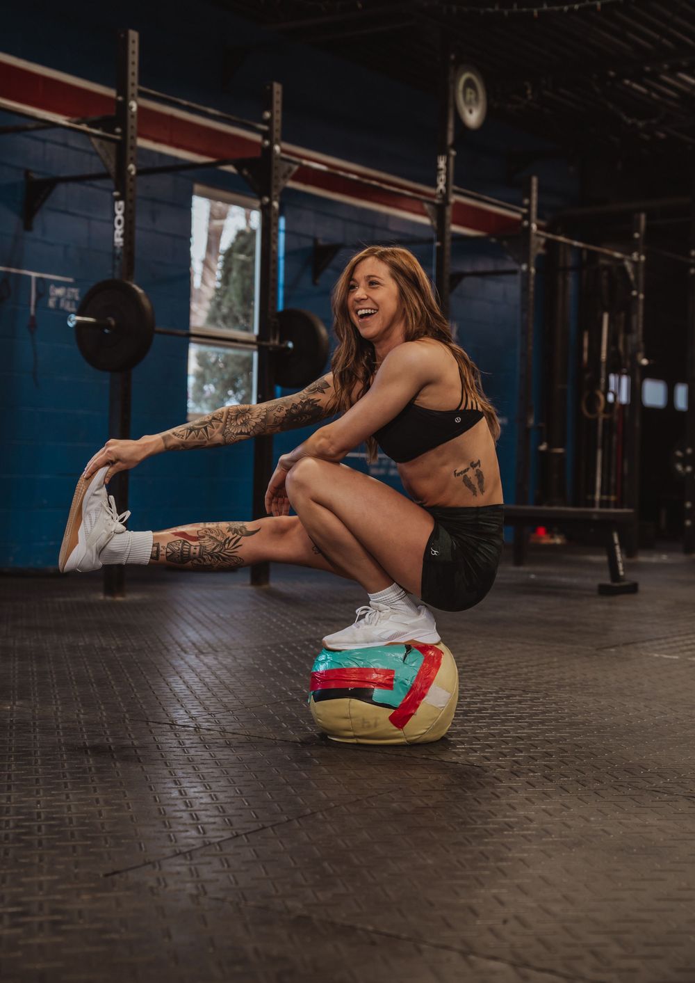 Fitness enthusiast stretches on rubber gym floor wearing colorful socks and white shoes. Female Crossfit athletes