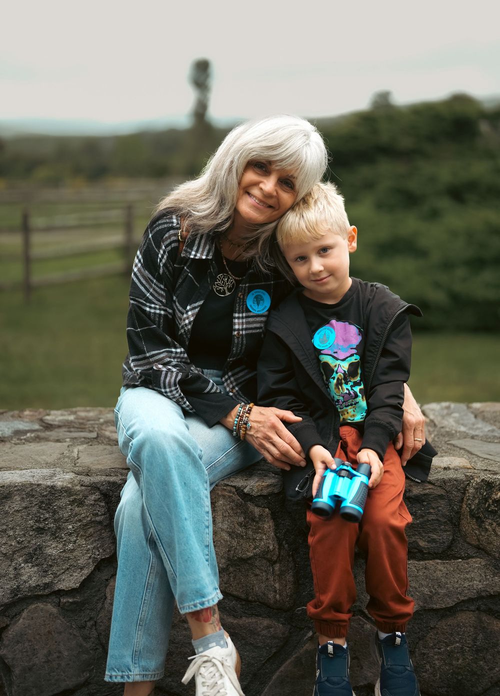 Two people sit together on stone wall outdoors sharing tender moment.
