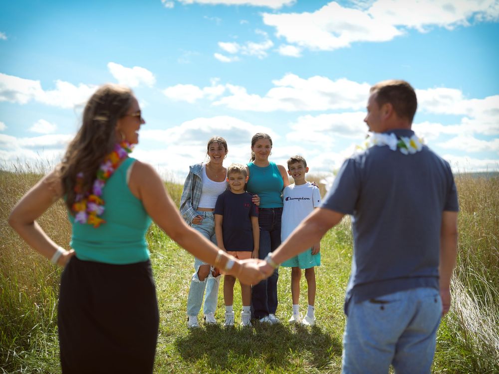 Group of people standing in a line in a sunny field with blue sky and white clouds.