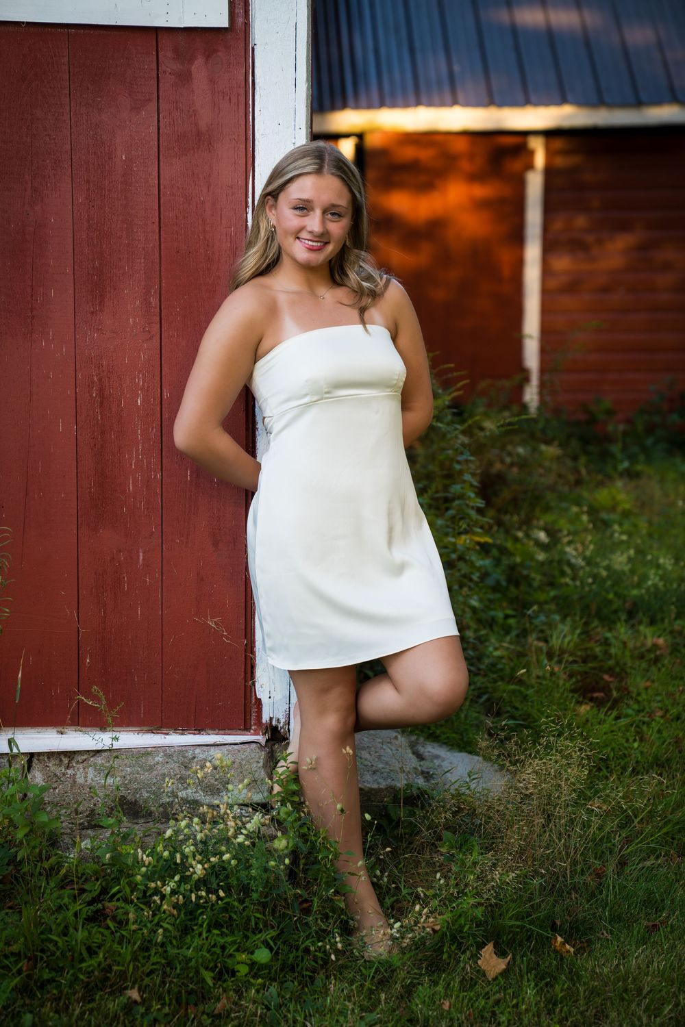 Playful pose by red barn wall with grass in foreground.