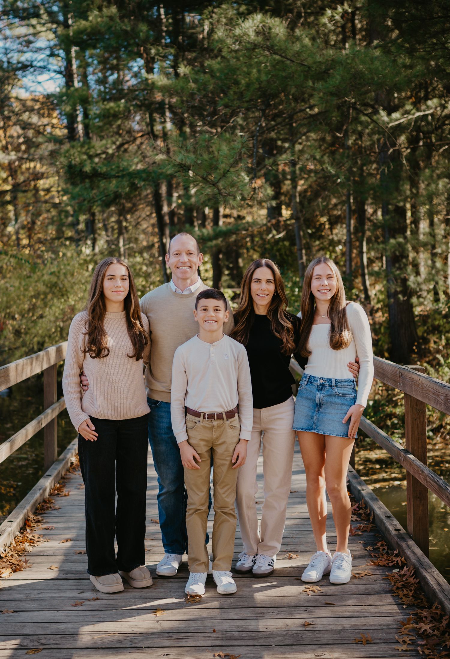 Family of six posing together on a wooden bridge surrounded by autumn forest trees in a warm fall portrait.