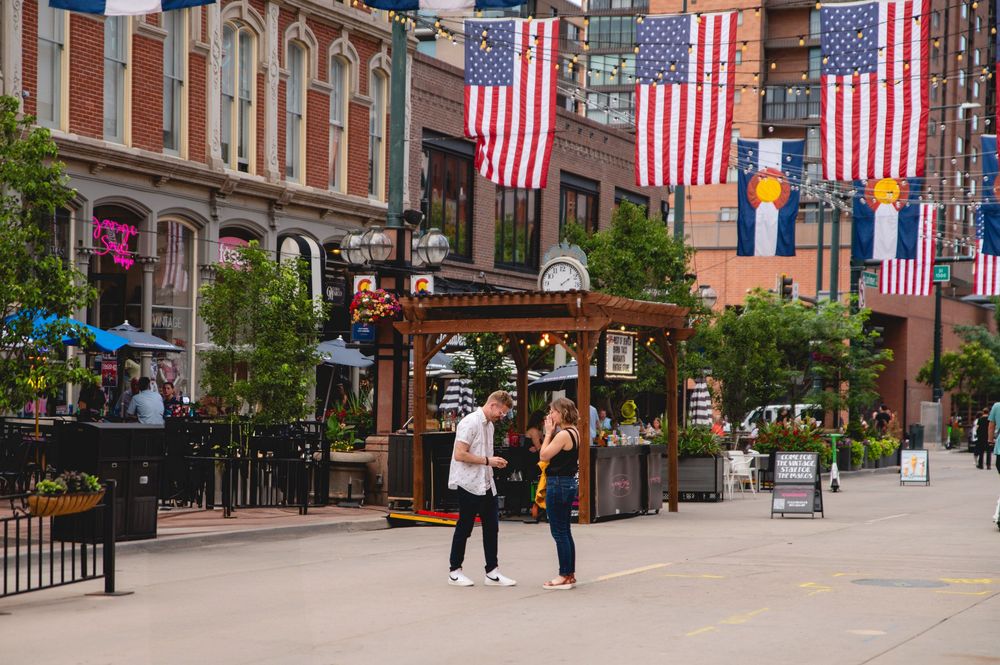 People walking along a charming downtown street decorated with American flags and historic brick buildings.