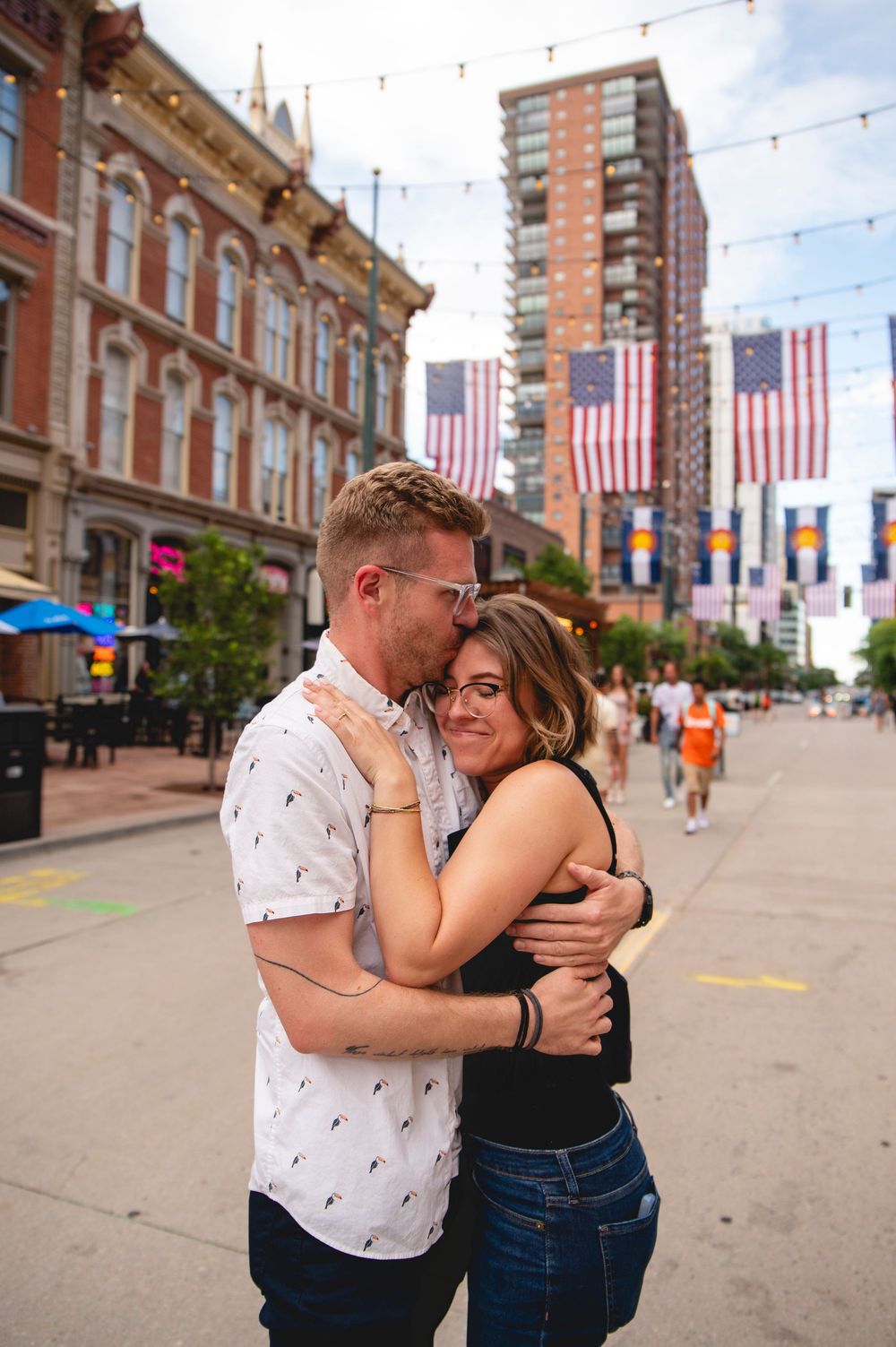 Couple sharing tender moments together on a city street decorated with American flags and string lights.