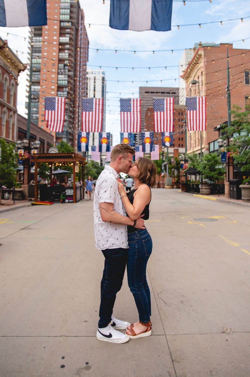A couple shares romantic moments on a brick street decorated with American flags and string lights.