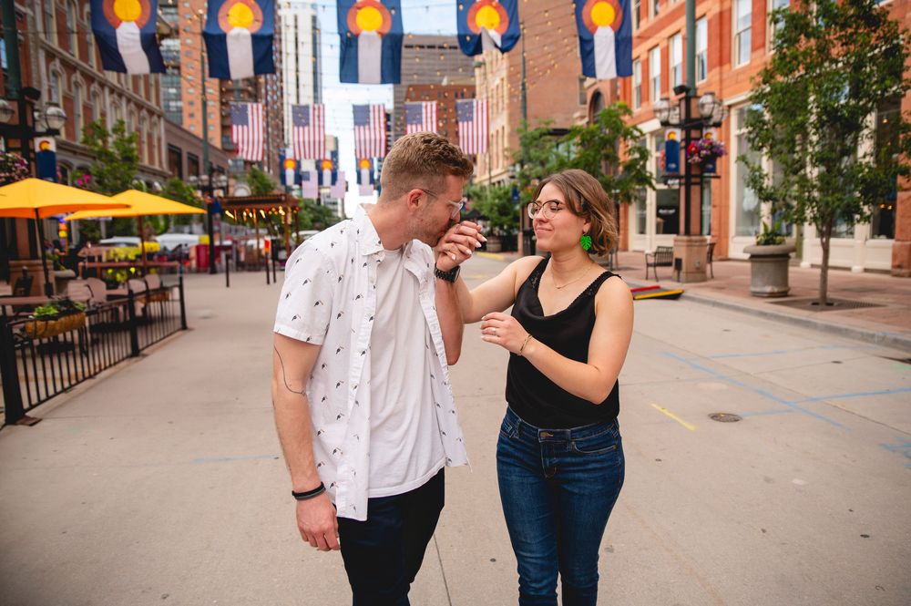 A couple shares drinks and conversation at an outdoor restaurant patio on a sunny urban street.