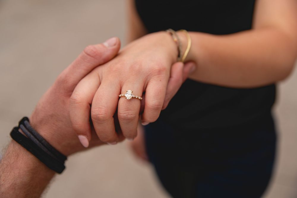 Close-up photo of two hands clasped together, with an engagement ring prominently displayed on one hand.
