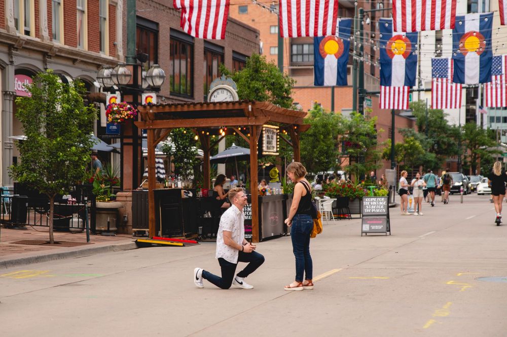 American flags line a city street with historic brick buildings and pedestrians enjoying a sunny day.