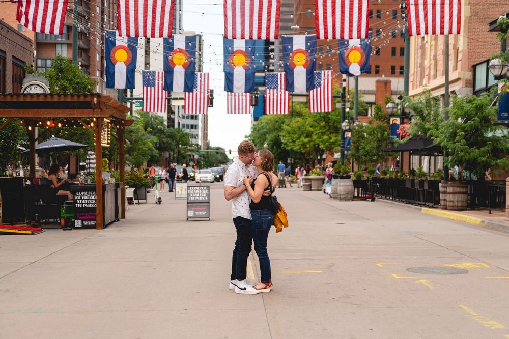 A couple embraces on a city street decorated with American flags and Pride banners in Larimer Square, Denver.