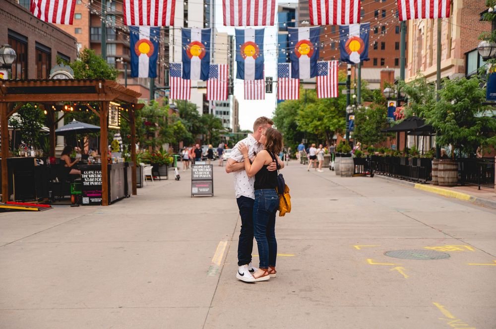 Colorful American flags line a bustling pedestrian shopping street with shops and buildings visible on both sides.