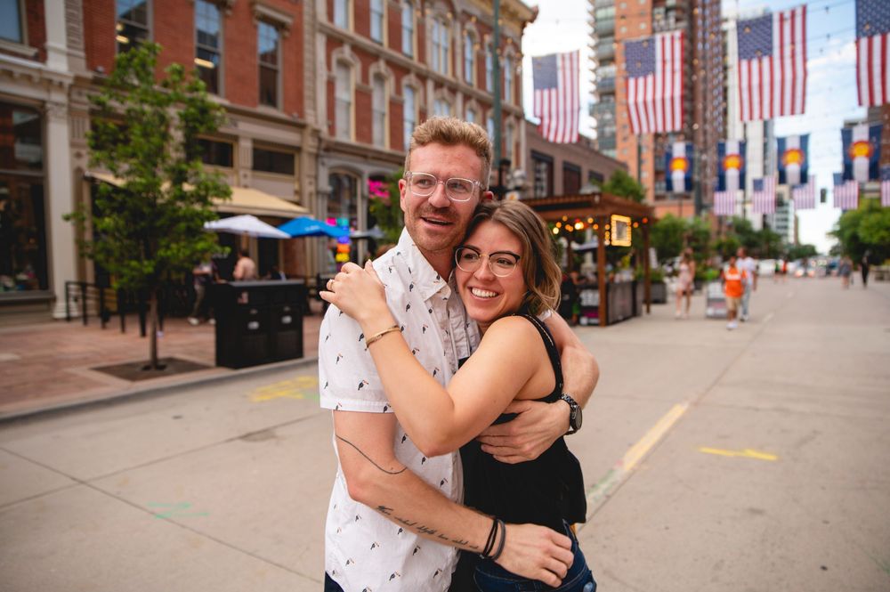 Two people embracing on a city street with American flags hanging from buildings in downtown area.