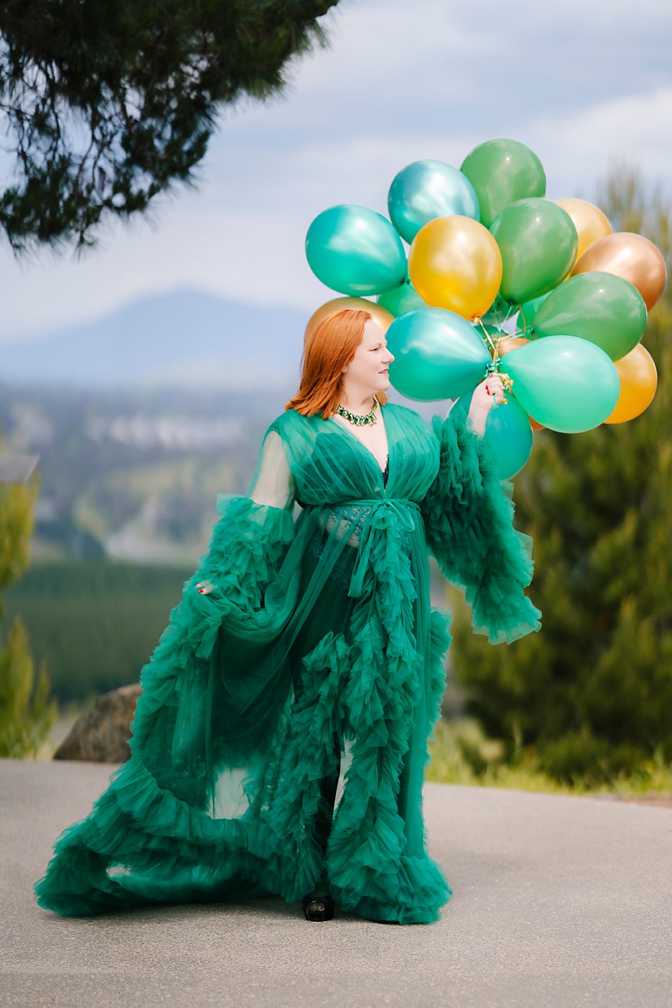 Emerald tulle dress with gold and green balloons creates a whimsical outdoor photoshoot scene.
