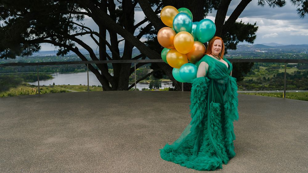 A scenic mountain photoshoot featuring a green gown and festive balloons against a dramatic landscape.