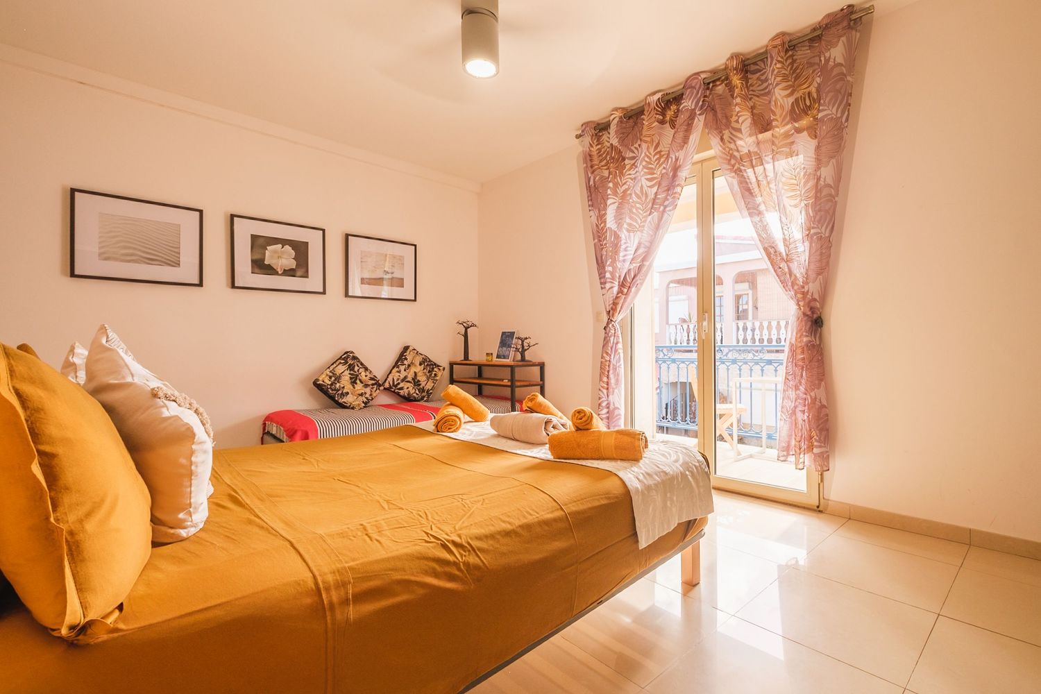 Modern bedroom interior with pale pink curtains, yellow bedding, and minimalist white walls and decor displays.