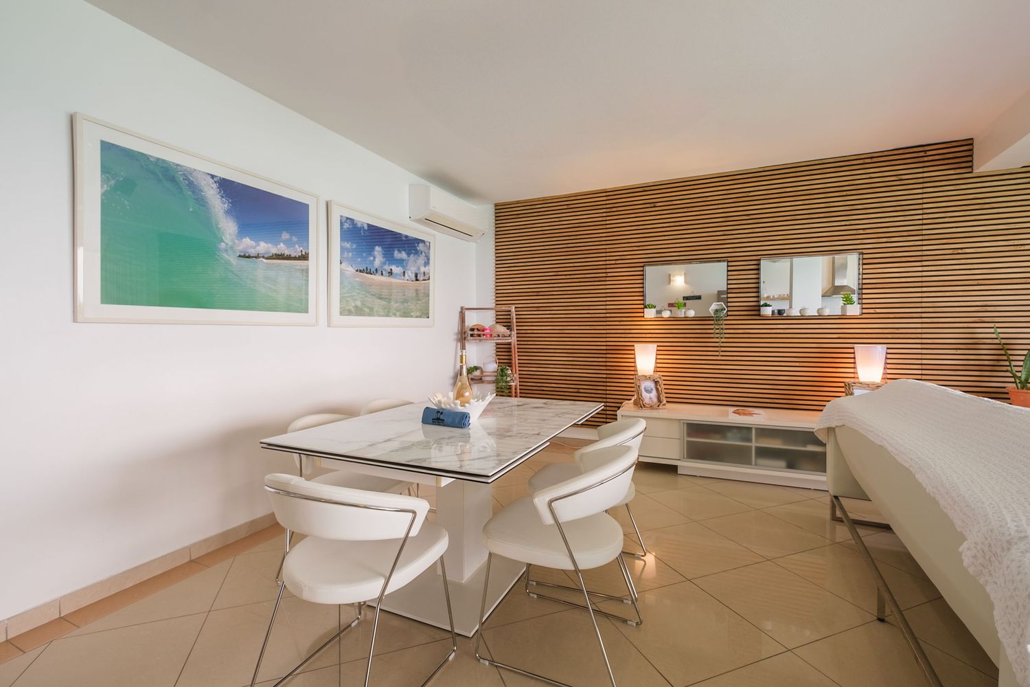 Modern hotel room interior with white dining area, wood accent wall, and coastal artwork displaying beach scenes.