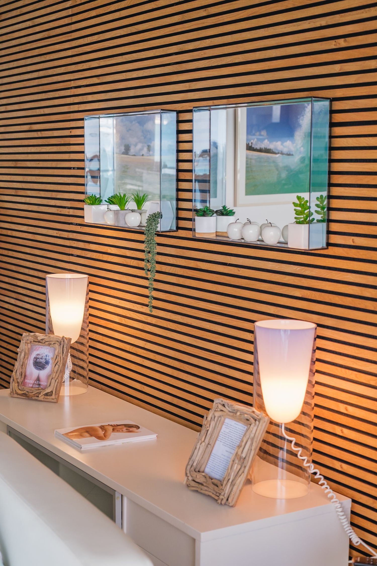 Modern wooden slat wall with accent lighting and white shelf displays decorative items in a minimalist design.