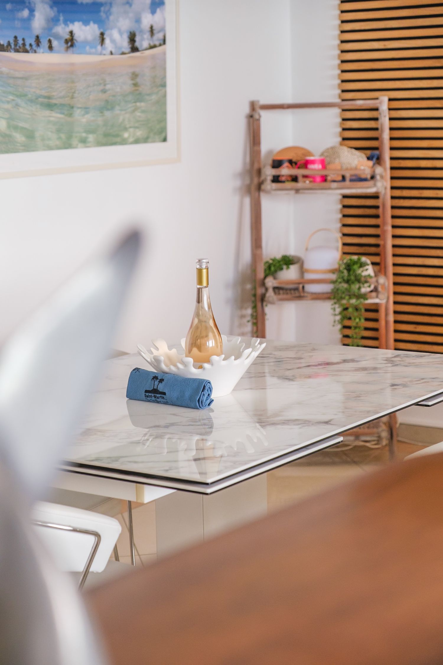 A white marble dining table with a wine bottle, blue napkin, and wooden decor elements in a modern interior setting.