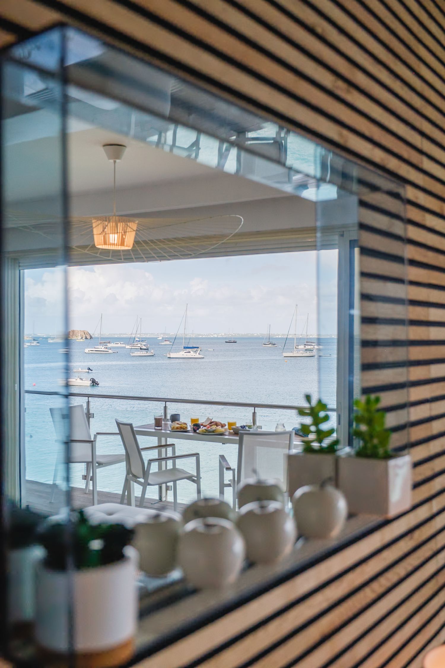 Modern restaurant interior with panoramic ocean view through large windows framed by wooden slat walls.