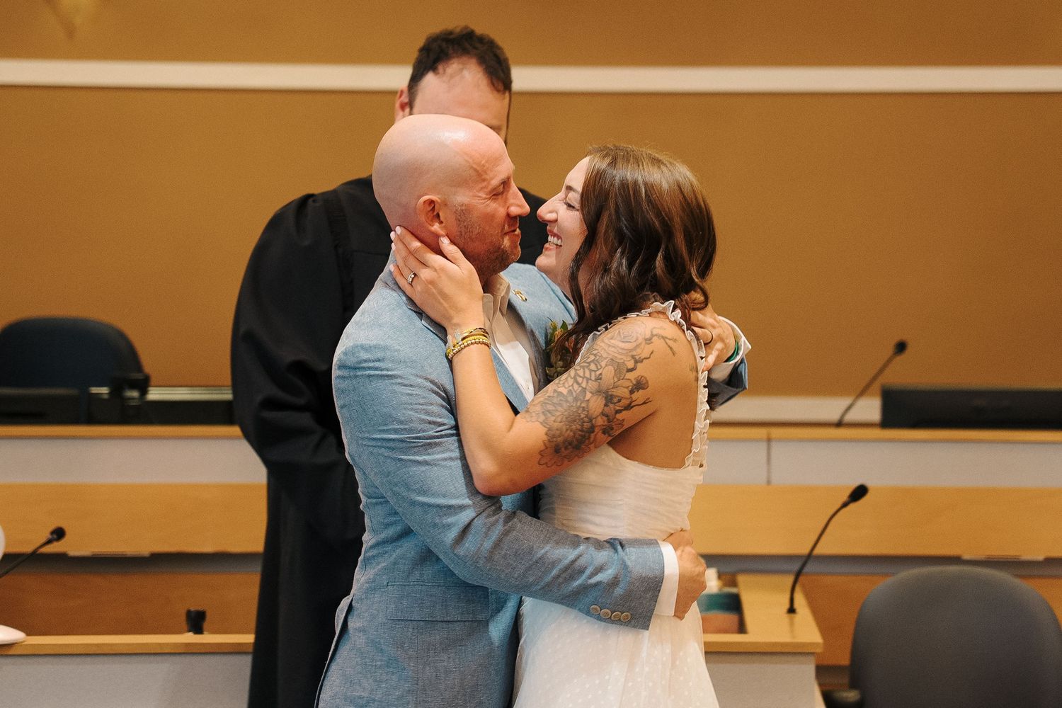 Newlywed couple shares a romantic kiss in front of a wooden backdrop at a wedding reception venue.