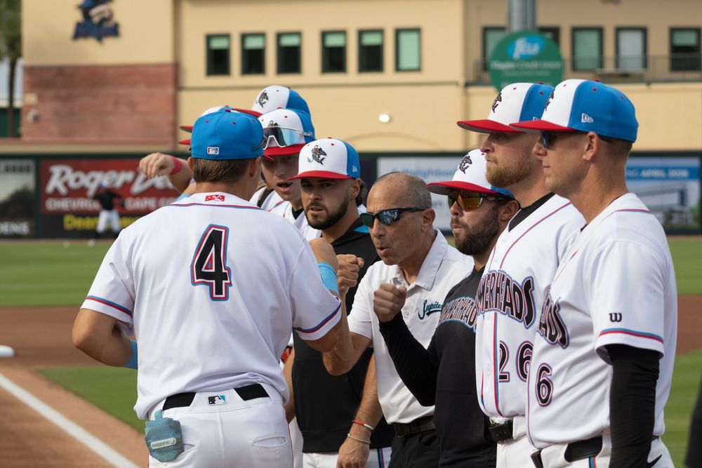 Baseball team members line the dugout railing during a minor league matchup.
