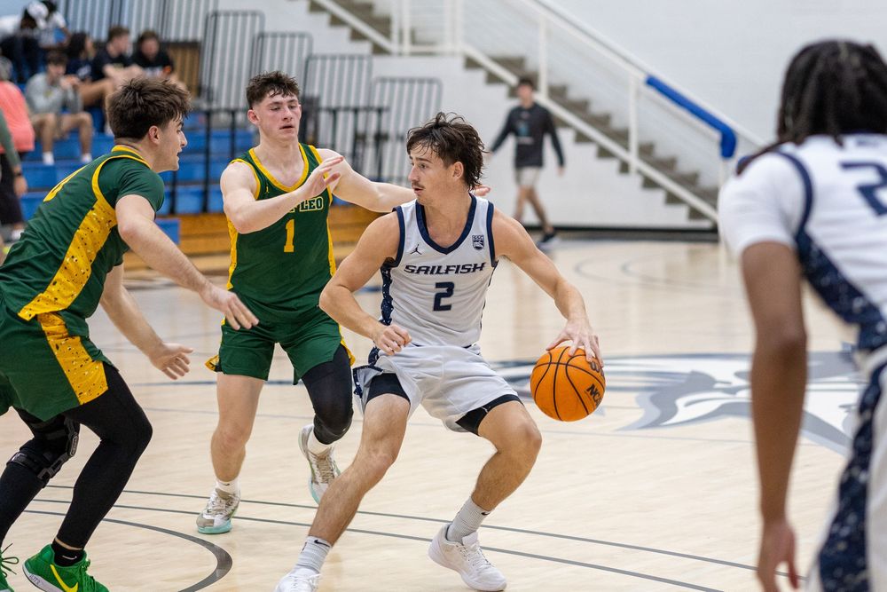 Basketball player dribbles past defenders during intense game action.