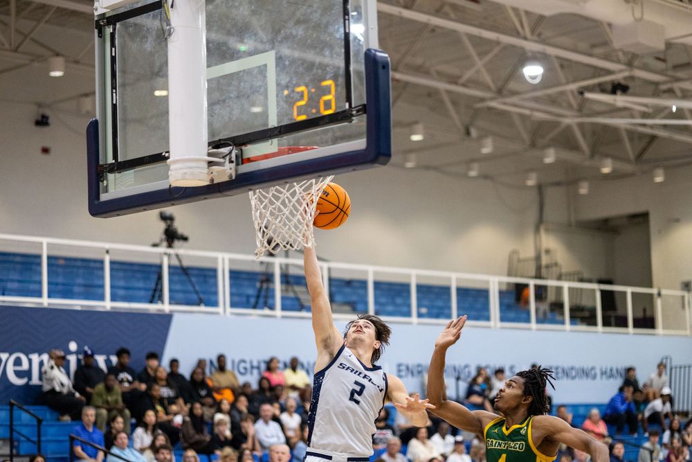 Player attempts layup during competitive basketball game with defenders nearby.