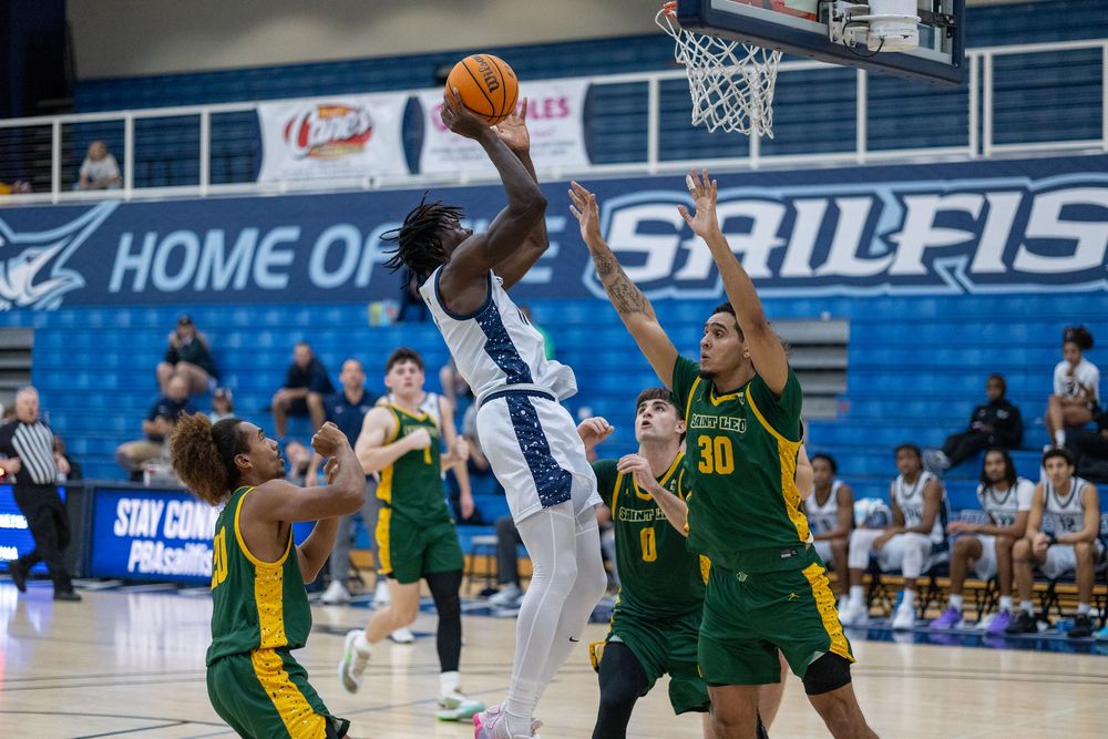 Basketball player leaps high for shot while surrounded by defenders in green jerseys.