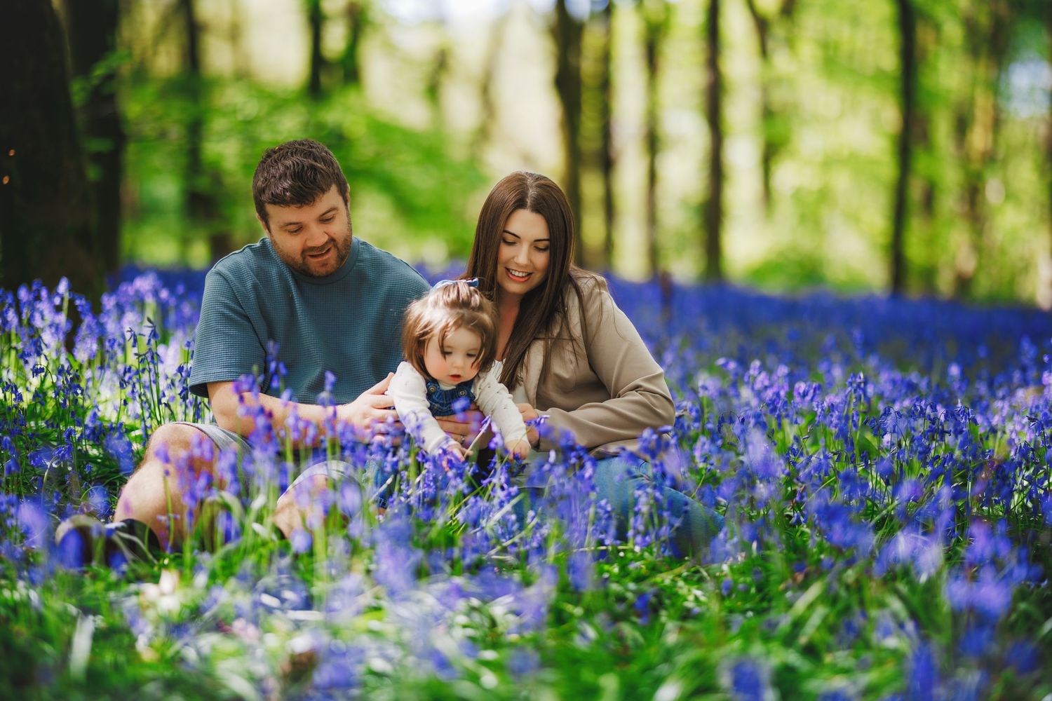 A family enjoys a spring day together among beautiful purple bluebells blooming in a lush forest setting.