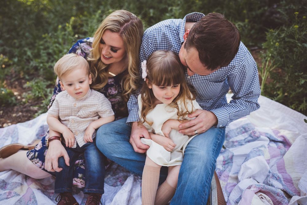 A joyful family shares tender moments together while sitting outdoors in a forested setting during a photo session.