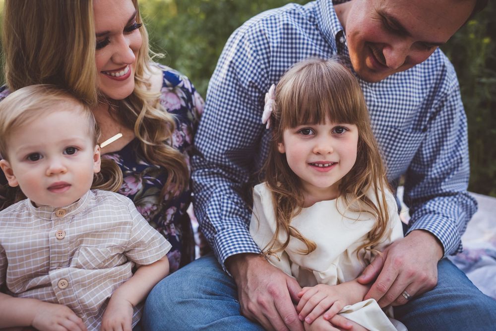 A young family sits close together outdoors while smiling and bonding during a portrait session.