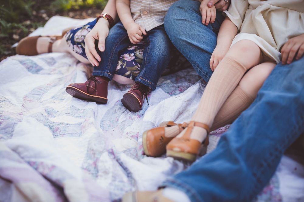 People sitting together on a picnic blanket while wearing casual shoes and jeans in an outdoor setting.