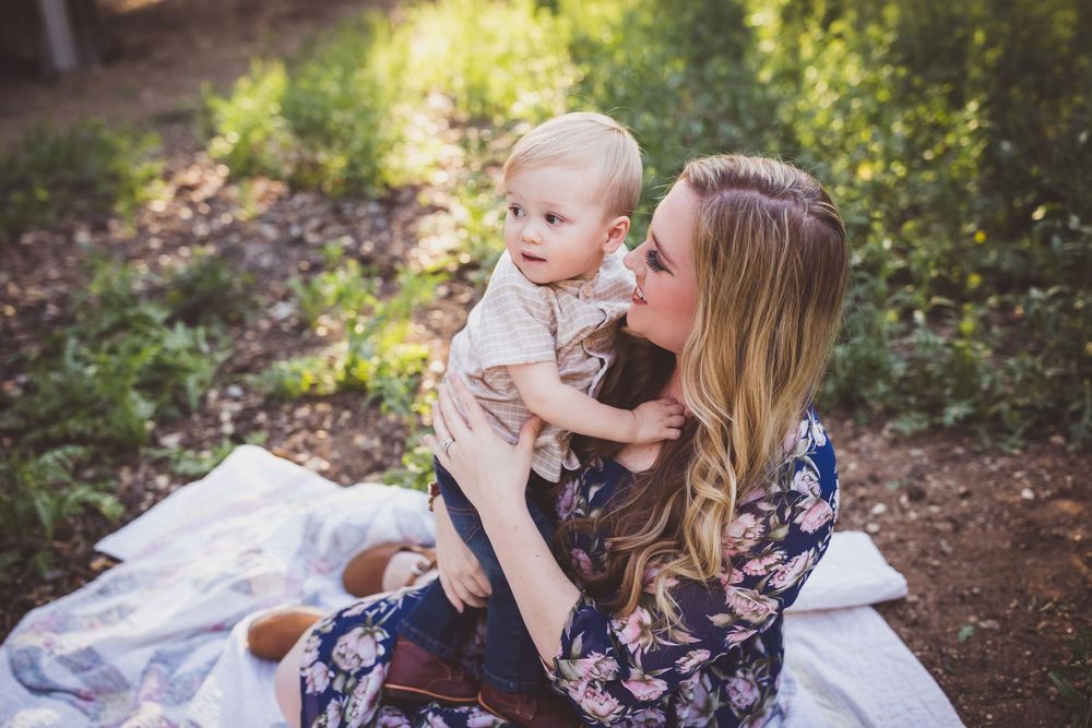 A touching family portrait session outdoors shows tender moments and cuddles on a blanket in a wooded setting.
