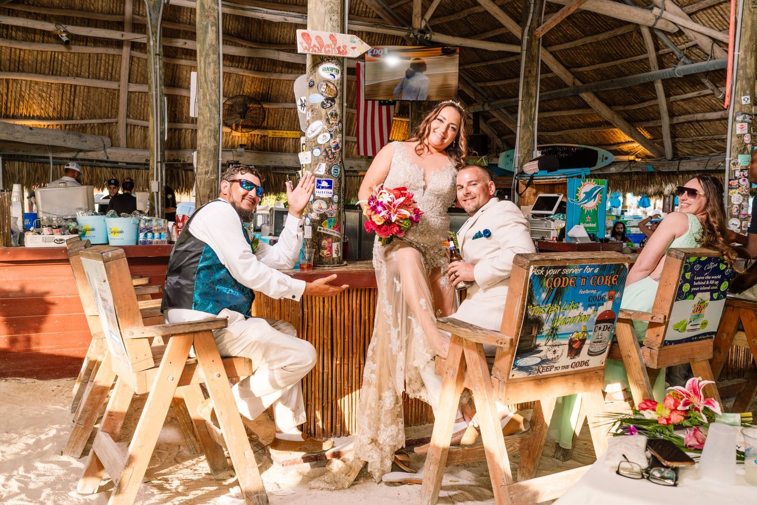 Wedding celebration in rustic wooden pavilion with turquoise chairs and festive decorations at casual beach venue.