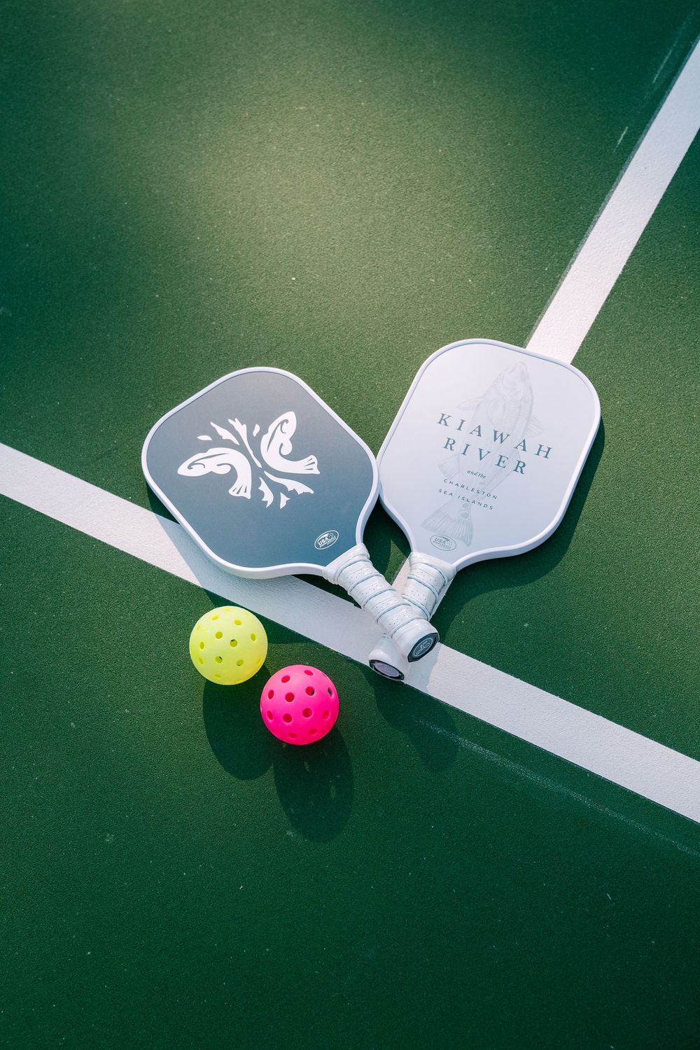 Two pickleball paddles and colorful balls on green court surface.