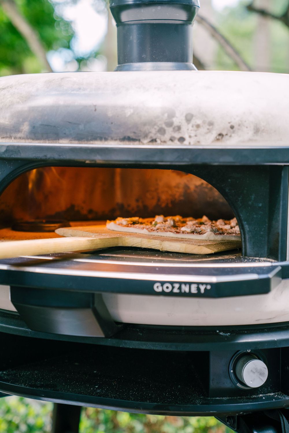 Close-up view of a black outdoor pizza oven with food cooking inside showing multiple cooking stages.