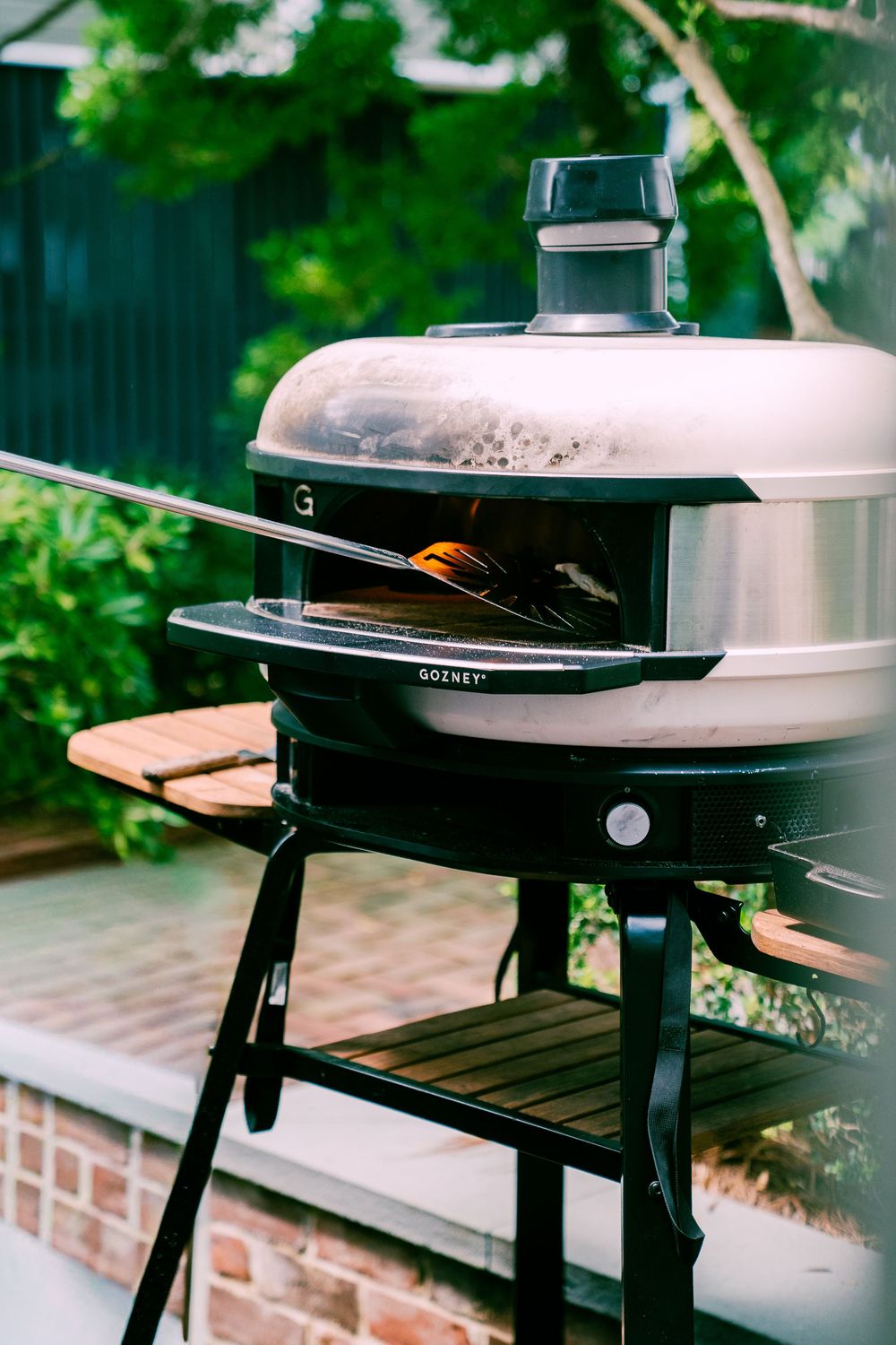 A series of outdoor grill cooking surfaces shown in progressive angles on a patio near green foliage and brick walls.