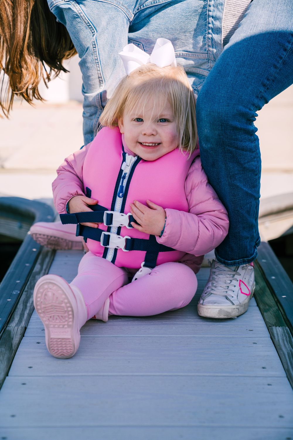 A child in a pink winter outfit sits on gray wooden steps in a series of four similar photos.