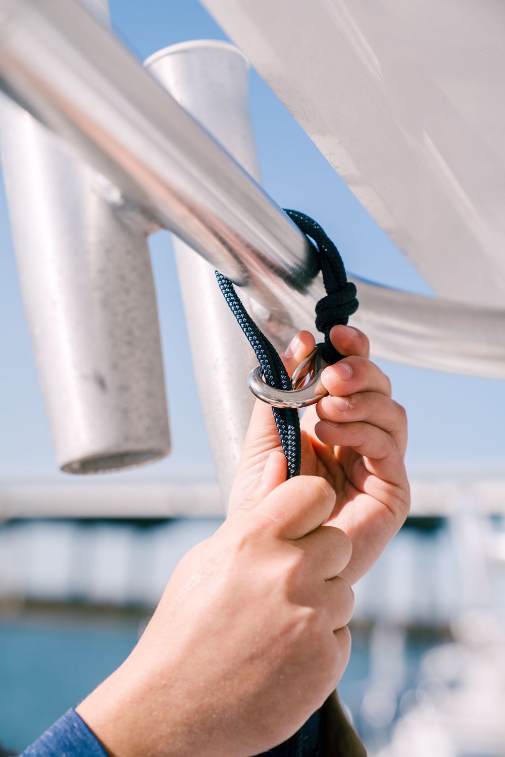 Close-up sequence of hands adjusting white sail rigging against a bright blue sky background.