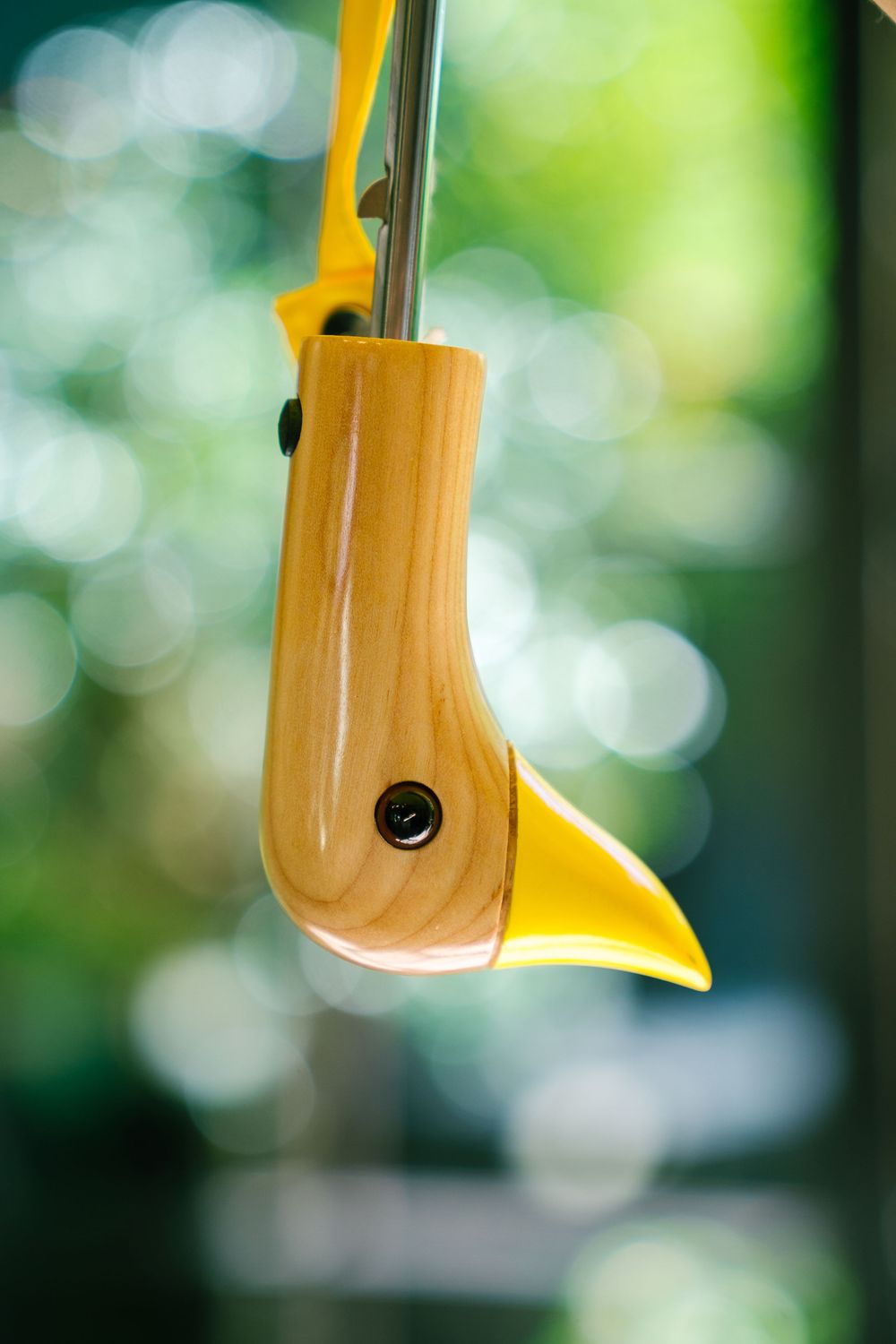 Close-up of yellow bird-shaped feeder against blurred green background.