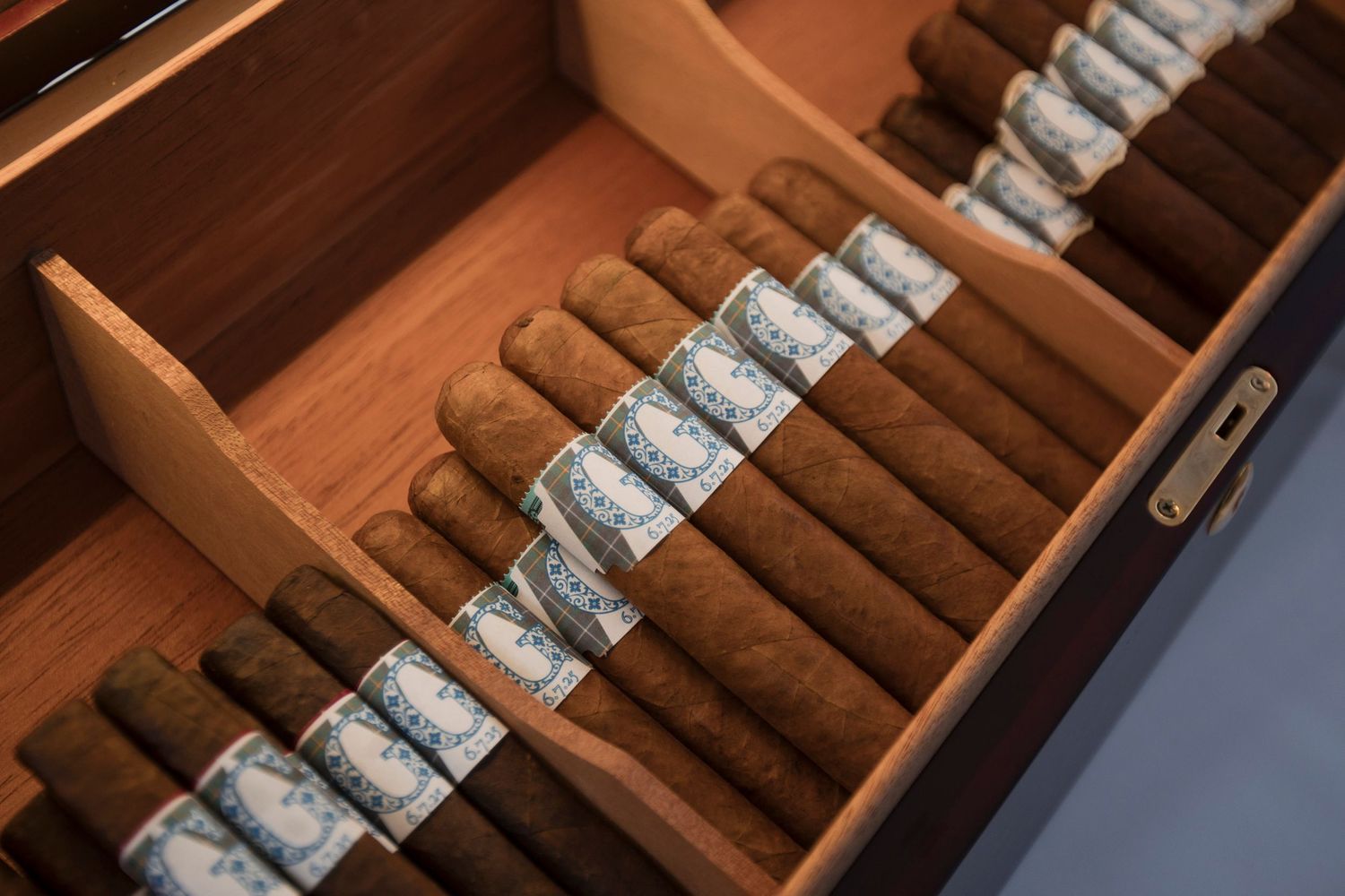 Premium hand-rolled cigars with silver labels arranged neatly in a wooden humidor drawer.