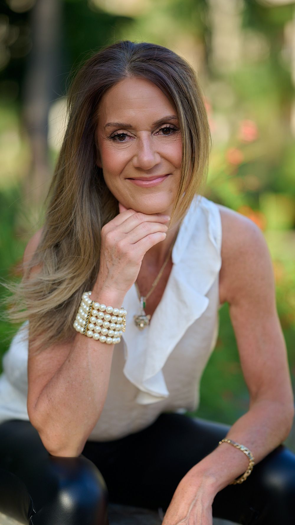 Professional portrait showing a sleek white blouse and pearl bracelet against a natural outdoor background.