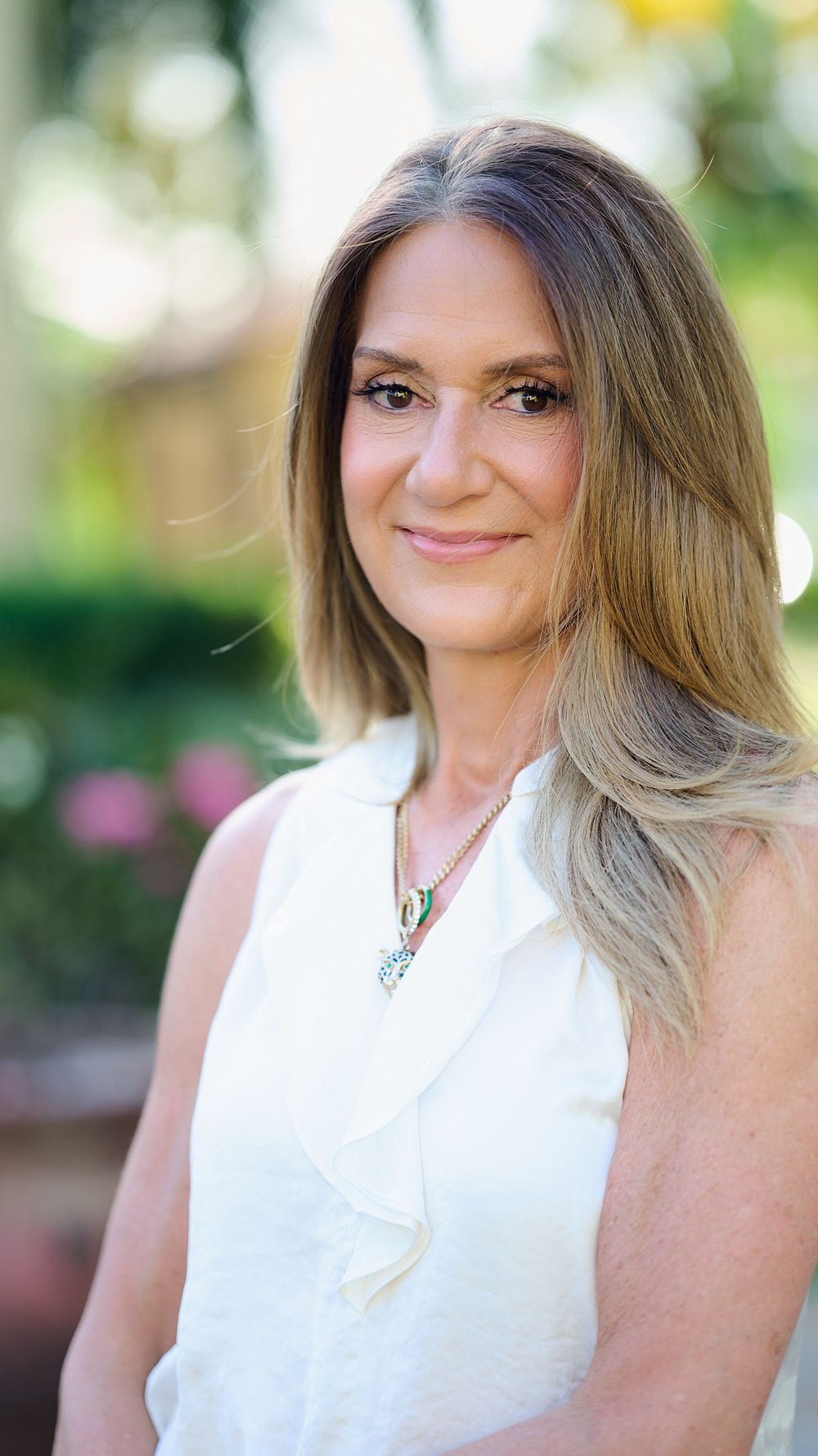 Elegant outdoor headshot featuring a white sleeveless top and delicate necklace.