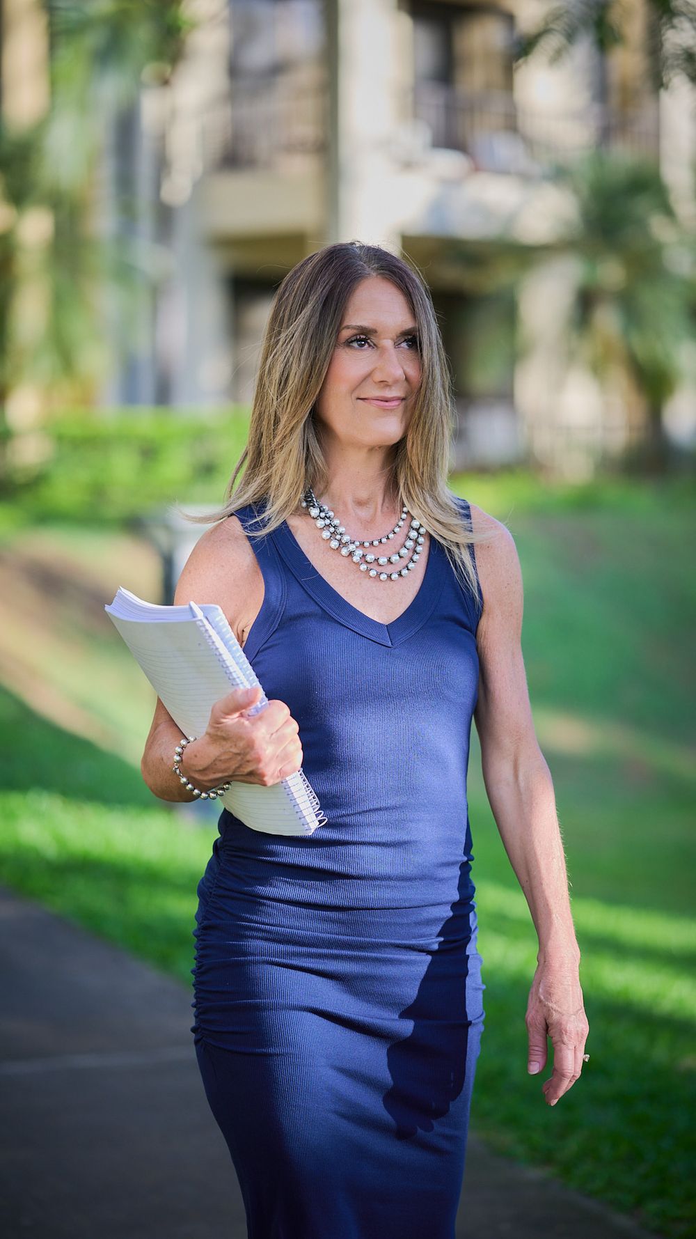 Professional wearing a fitted navy dress and statement necklace while holding documents outdoors.
