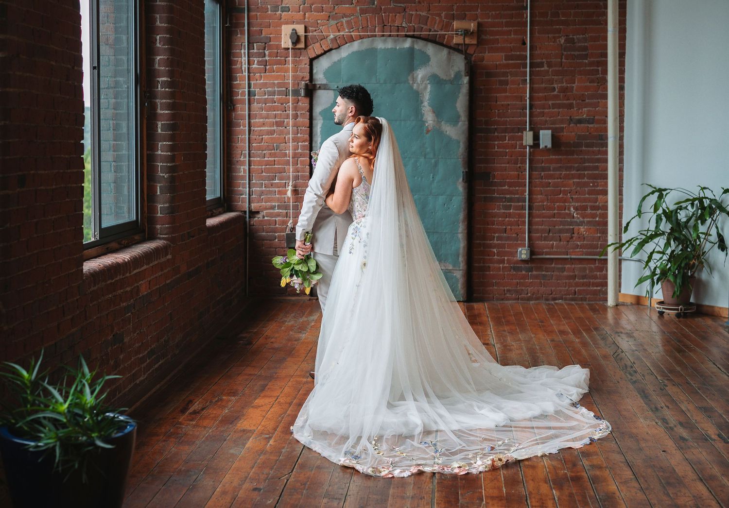 Candid moment at Mill 1 Holyoke. Bride in white gown with long veil embraced by groom in brick loft venue with hardwood floors.