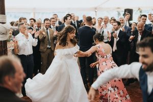 Newlyweds and guests celebrate on a dance floor at an outdoor wedding reception with a lively crowd.