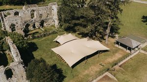 Aerial view of ancient stone ruins with modern shade canopy and green lawn on a sunny day.