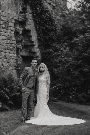 A black and white wedding portrait of a couple standing against an ancient stone wall with trailing ivy.