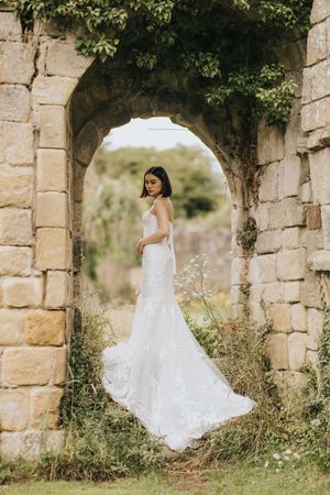 A white lace wedding dress photographed in an ancient stone archway covered in ivy and greenery.