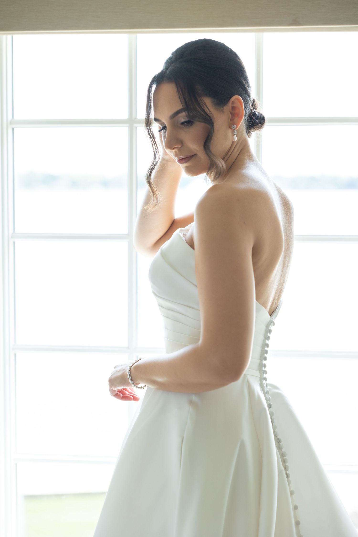 A series of photos showing someone adjusting a white strapless wedding dress near bright windows.