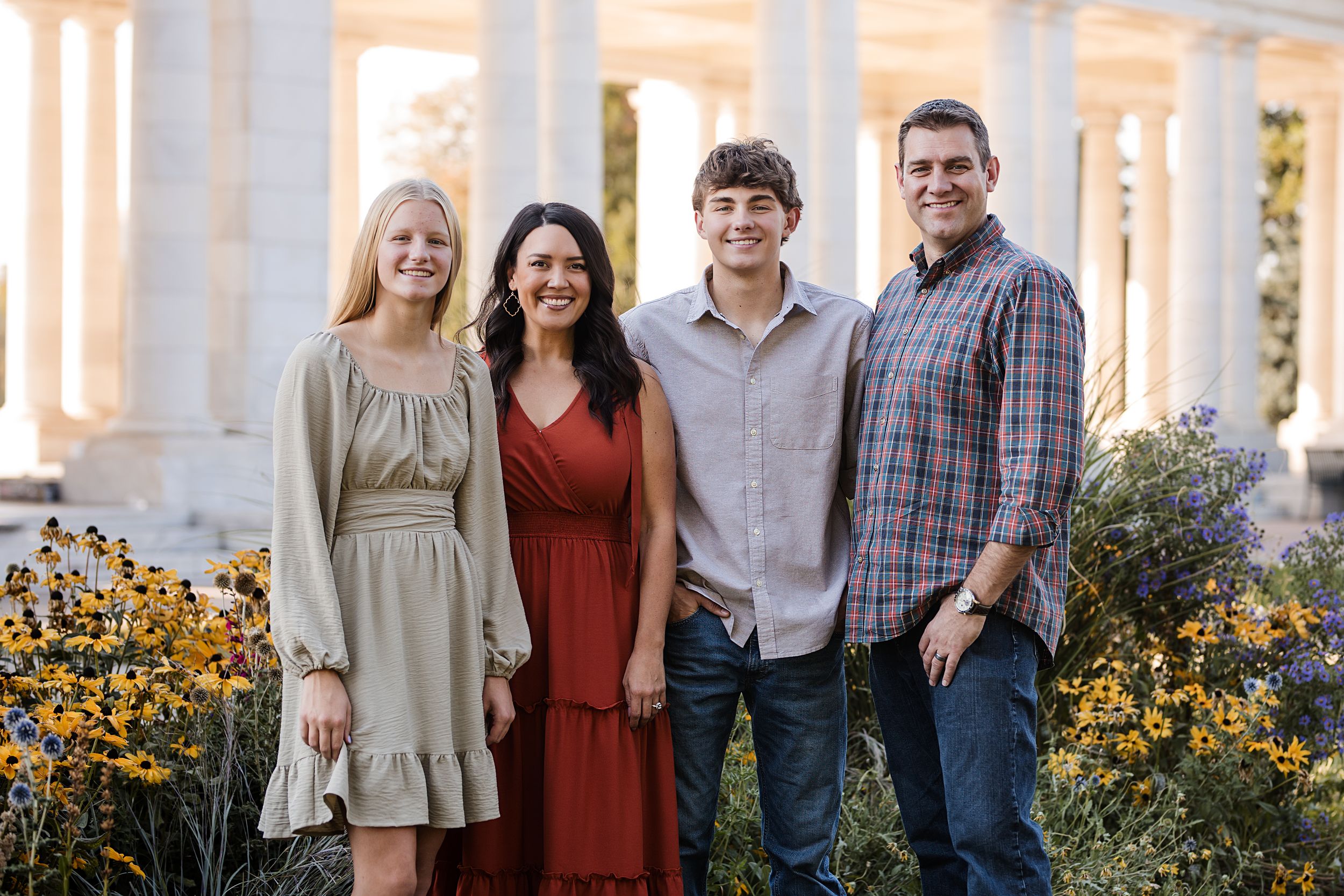 A group poses together by white columns with yellow flowers blooming in the garden.