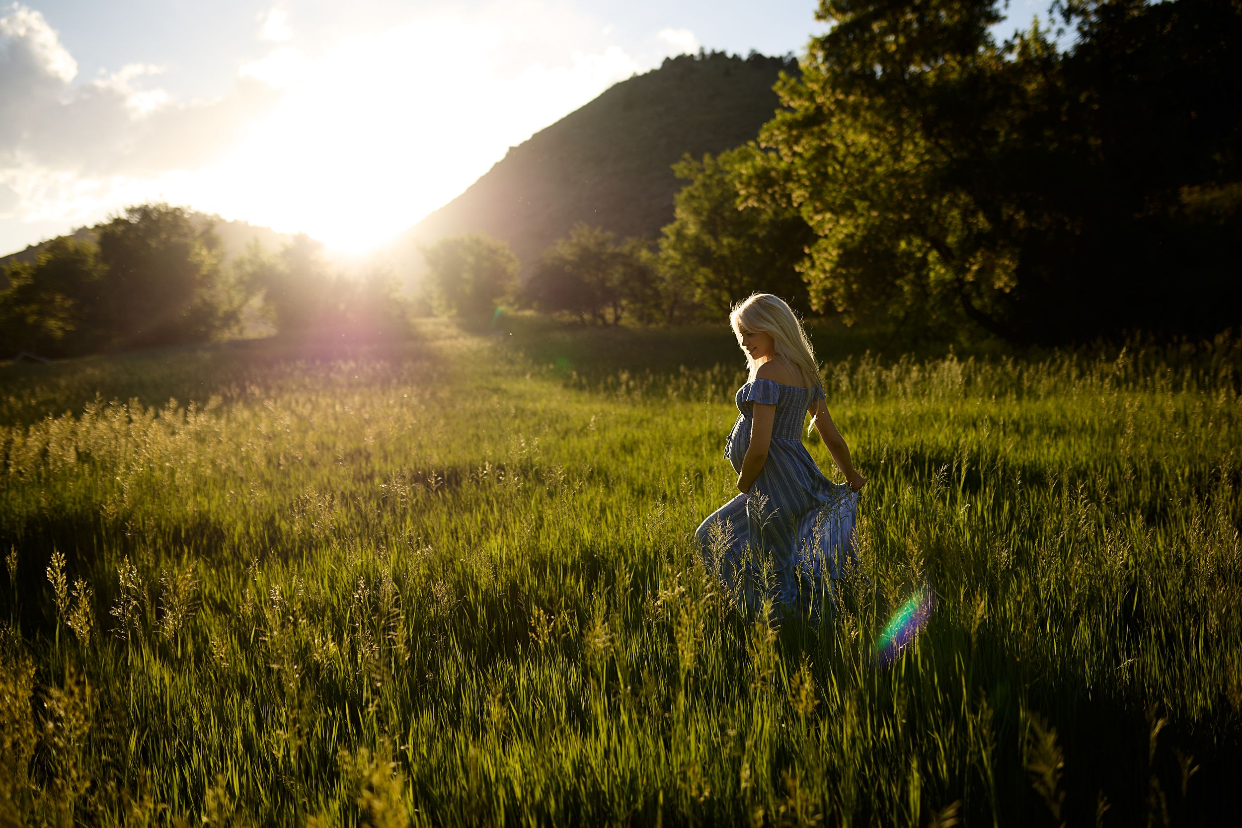 Silhouette of someone walking through a sunlit grassy meadow at golden hour with mountains in the background.